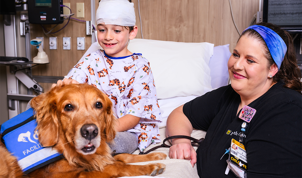 photo of a child in the hospital with a nurse and a golden retriever