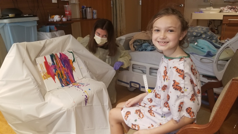 A girl smiling in front of a painting she's working on.