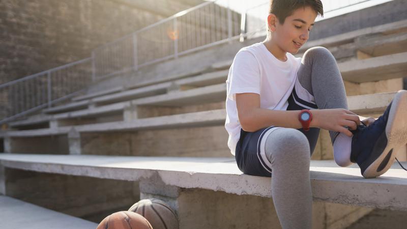 A teen tying his shoe, sitting on a stadium seat.