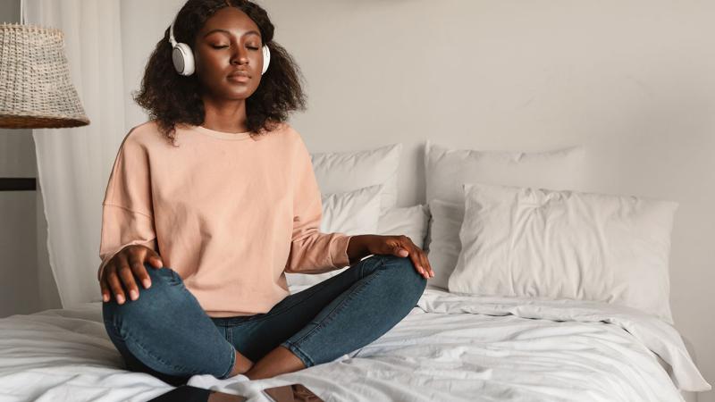 A woman meditating on the bed, listening to music.