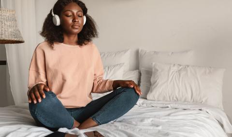 A woman meditating on the bed, listening to music.