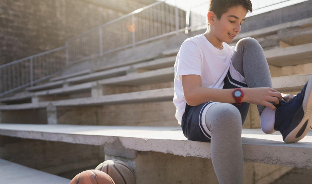 A teen tying his shoe, sitting on a stadium seat.